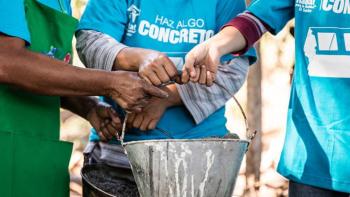 Three people holding a bucket handle.  The bucket has cement in it.