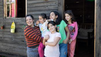 A woman in a orange and black striped shirt holding a little girls next to three more young girls in front of a house.