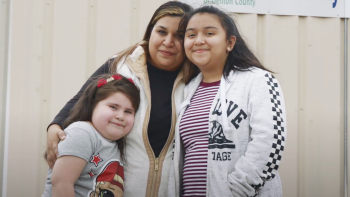 Dina smiling and embracing her two daughters.