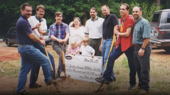 Group with shovels and large donation check on build site