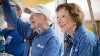 Jimmy and Rosalynn Carter in front of microphones smiling and waving