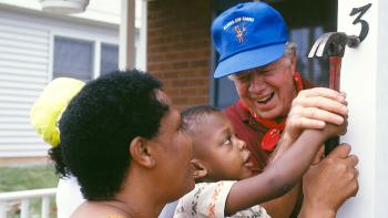 President Carter working with a child to hammer on his address number.