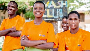 Three members of a school WASH club wearing branded Habitat for Humanity and My Legacy tshirts smile to the camera