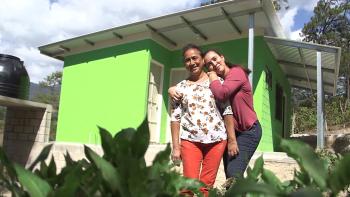 Two women hugging in front of their bright green home in El Salvador