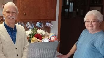 Smiling elderly couple standing in their kitchen with large gift basket