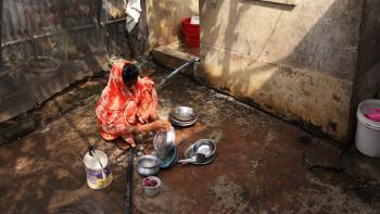A woman in colorful, orange clothing washing dishes outside.