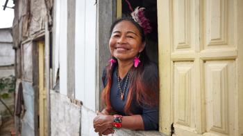 A woman smiles from a window with yellow panes.