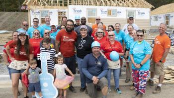 Group of smiling volunteers in front of framed house on build site