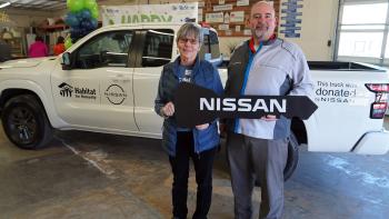 Two people holding a giant prop key that says "Nissan" standing in front of a white Nissan truck with the Habitat for Humanity logo. 