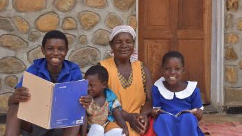 A woman and three children sit outside their home smiling