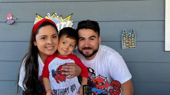 Mother, son and father posing in front of spiderman birthday decorations.