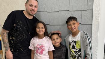 Father in a black shirt posing with three children, a young girl and two young boys.