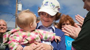Mrs. Rosalynn Carter holding a baby, smiling a crowd of volunteers.