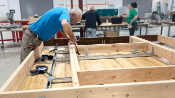 Man in blue shirt works on building a pre-fab wall panel inside a warehouse.