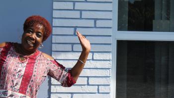 A woman poses joyfully by a wall of white bricks.