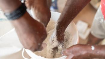 Multiple hands reach into a bucket to help mix a building material.