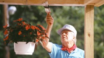 President Carter painting a porch roof, wearing a cap and red bandana.