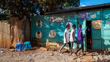 Three young kids walk to a blue-colored shelter.