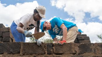 Two volunteers (woman, left) (man, right) in Habitat shirts and hats building a stone fence.