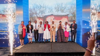 A group of people standing, clapping with a background of media screens