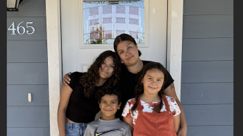 Mom, teenage daughter, young daughter and young son posing in front of a white door on a porch.