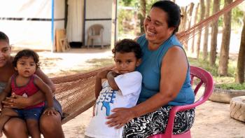 A mother holding her child, smiling outside her home in Honduras.