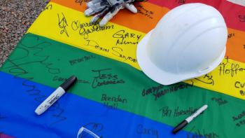 Photo of a signed rainbow flag with a hardhat on top.