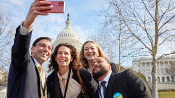 A group of four smiling for a selfie in front of the United States Capitol Building.