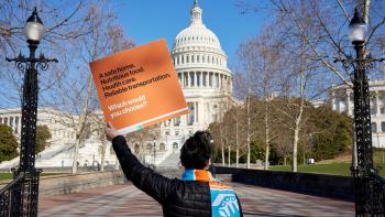 A woman holding an orange Habitat advocacy sign stands with her back to the camera as she looks toward the Capitol building in Washington D.C.