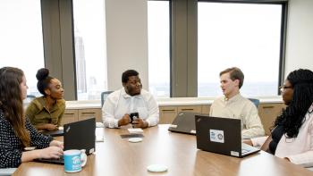 A group of young professionals sitting at a table together with laptops, holding a meeting in the Habitat headquarters office.