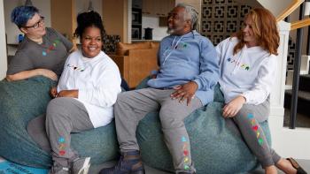 A group of four people smiling and laughing as they lounge on big bean bag chairs, swearing Habitat sweatshirts and sweatpants.