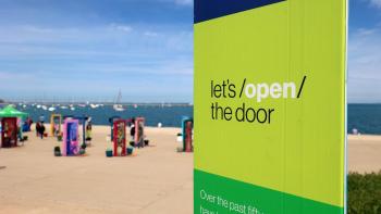 A branded column that says let's open the door in the forefront. In the background is a pop-up door installation displayed in front of a lake.