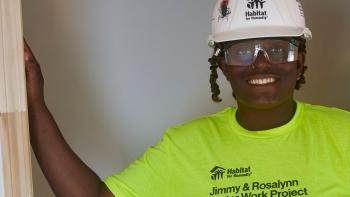 Amia stands with her arm in a doorway smiling at the camera.