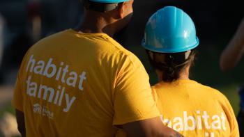 A pair of homeowners in yellow shirts that read, "habitat family," hugging during sunrise.