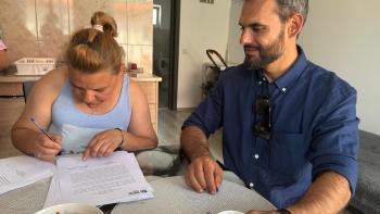CEO of Habitat for Humanity Romania sitting next to Mihaela, signing her house form
