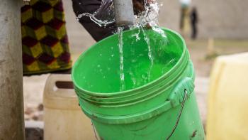 A woman fills up a green bucket with water from a kiosk.