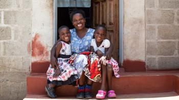 A Zambian woman hugs her two daughters on the front step of their brick home.