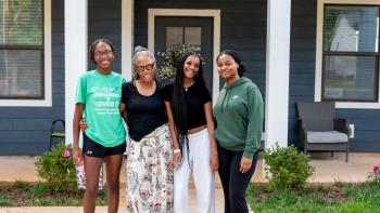 Grandmother and three teenage granddaughters posing in front of a navy and white house.