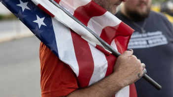 Veteran in red shirt carrying U.S. flag.