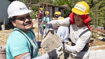 Two Global Village volunteers on a home build site holding a cement block