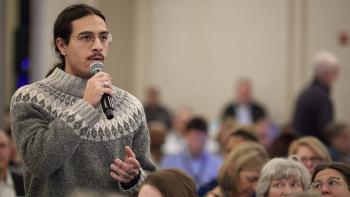 Person in a sweater speaks into a microphone in front of a crowd