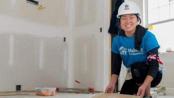 Young woman Collegiate Challenge volunteer smiling while working in an unfinished house.