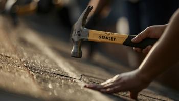 Close-up of hands hammering nails on a roof, with other people hammering in the background
