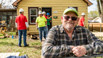Robert smiling in front of his home with Habitat volunteers in the background
