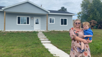 Woman holds her 2-year-old son in front of their Habitat home. 