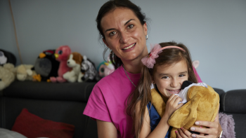 Young girl smiles and hugs a stuffed puppy toy while sitting with her mother on their couch.