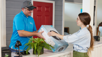 Man volunteering as a Habitat ReStore cashier wearing ReStore branded shirt and hat and helping woman buying items.