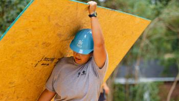 Woman volunteer in a hard hat carrying a sheet of plywood