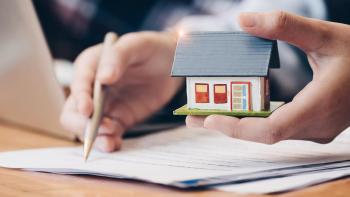 Hands holding a small model home and signing papers