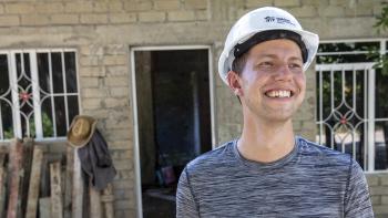 Young man wearting white hard hat and smiling in front of a concrete block home